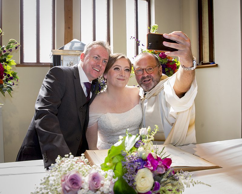 Bride and groom pose for selfie with priest